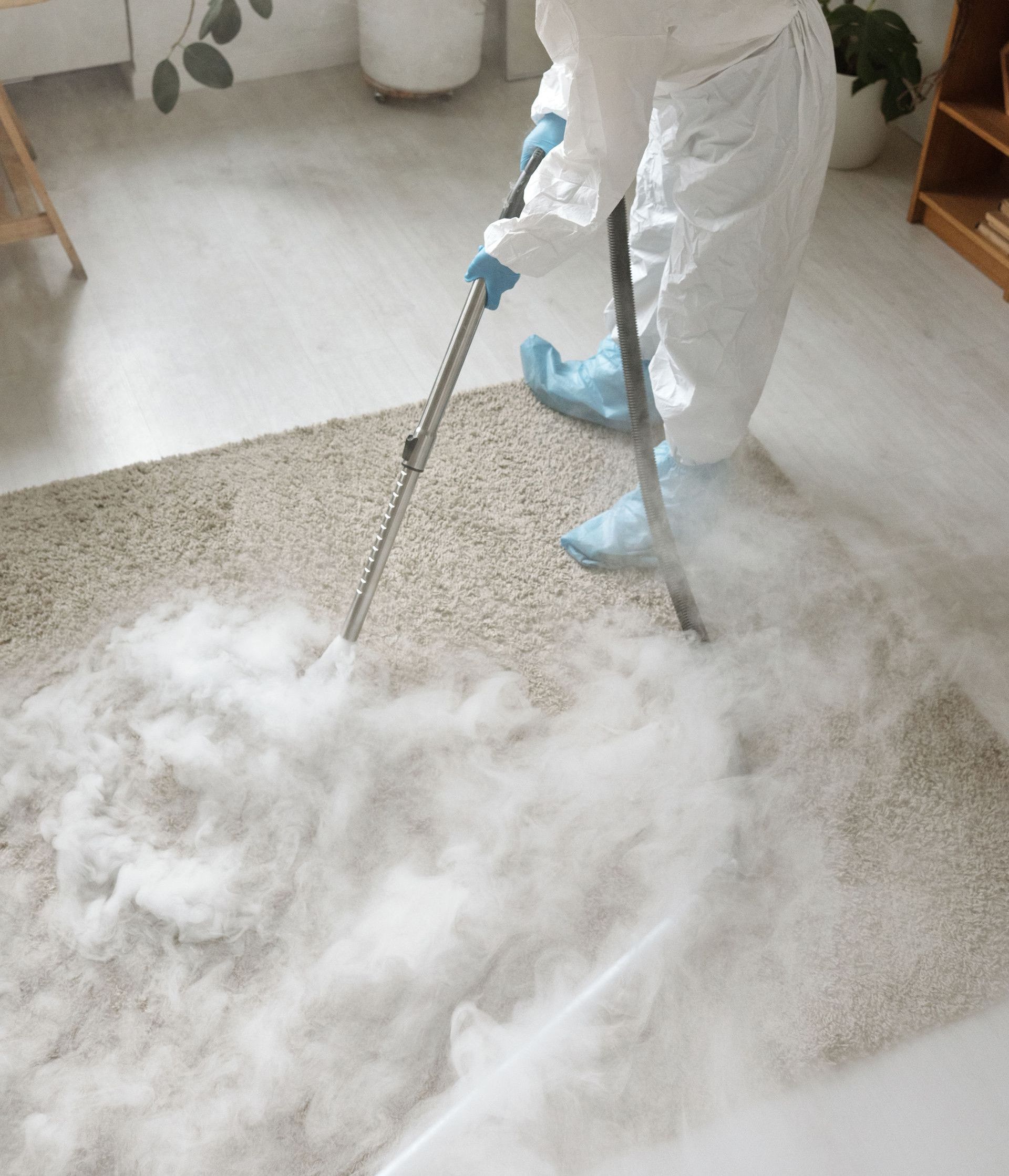 Woman in protective gear disinfecting a carpet indoors during COVID-19 pandemic.