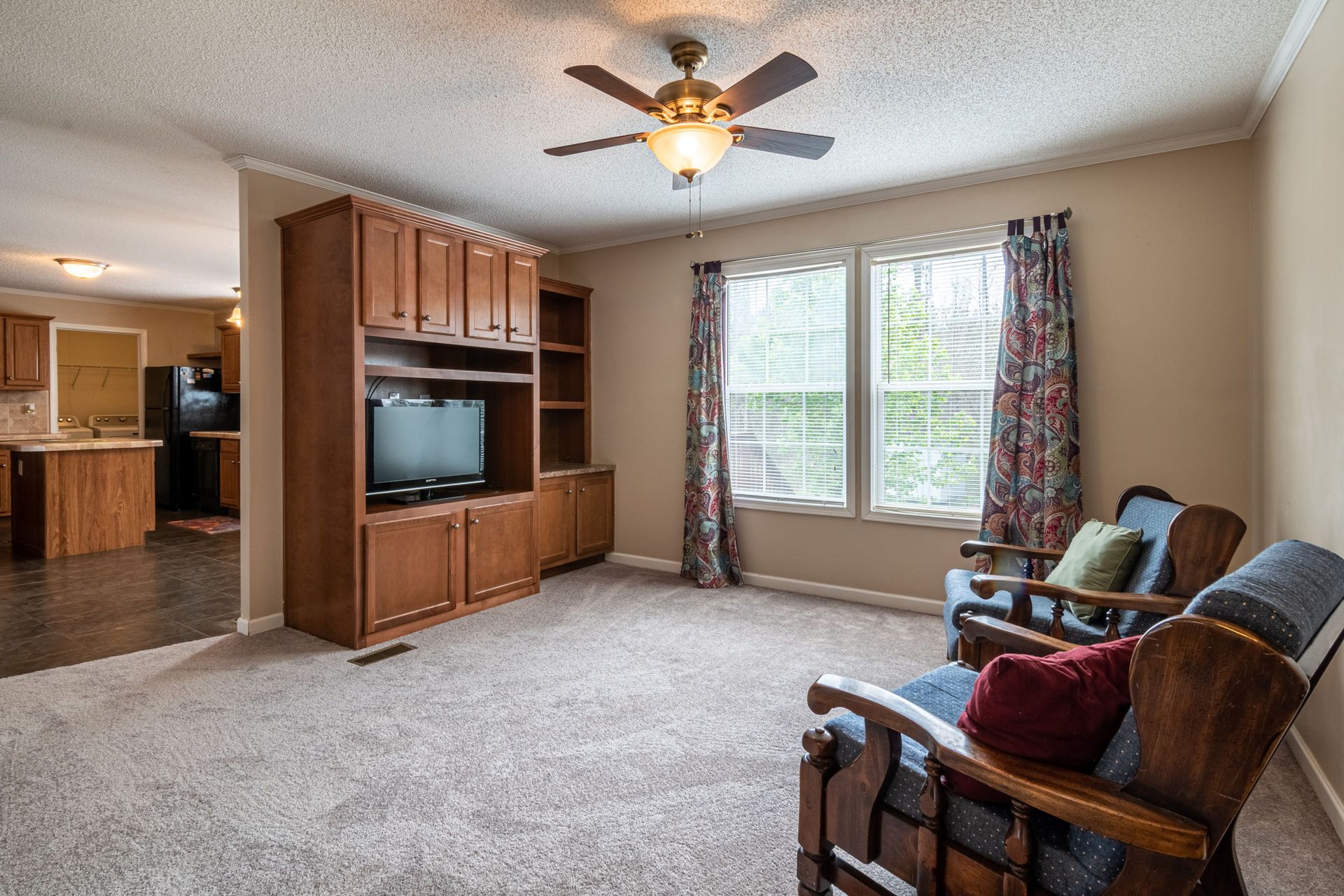 Spacious living room with classic wooden entertainment center and ceiling fan, perfect for a family setting.