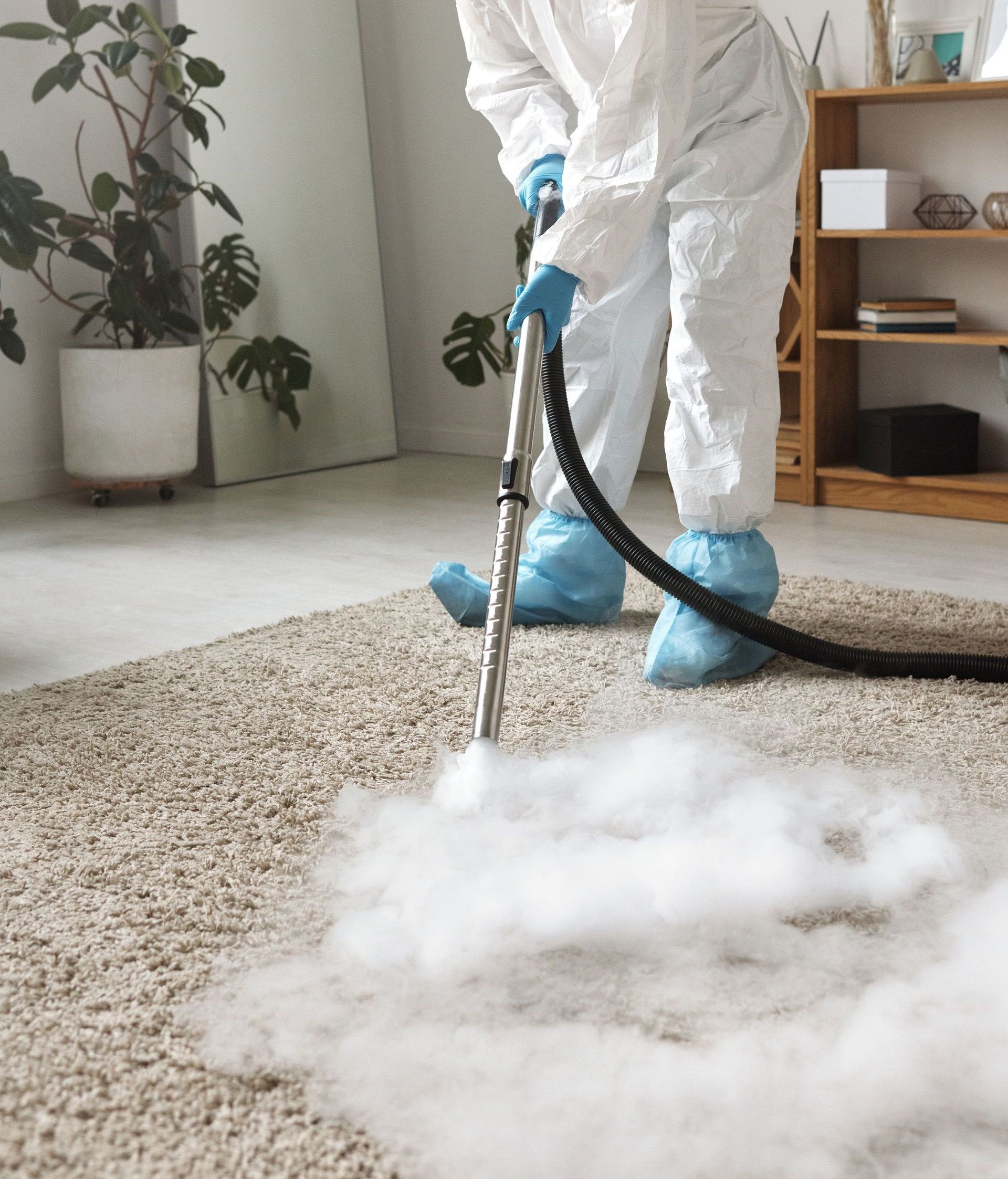 A person in protective gear disinfecting a carpet with a fumigation device indoors.